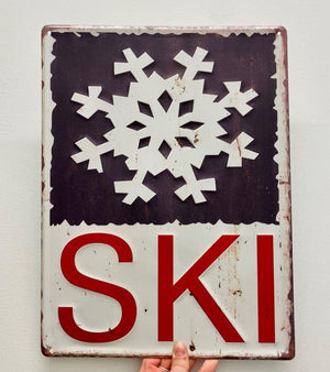 SKI Embossed Metal Sign. White Backgroud with 'SKI' in Red Font. Top Portion Features a Blue Background with an Embossed White Snowflake.