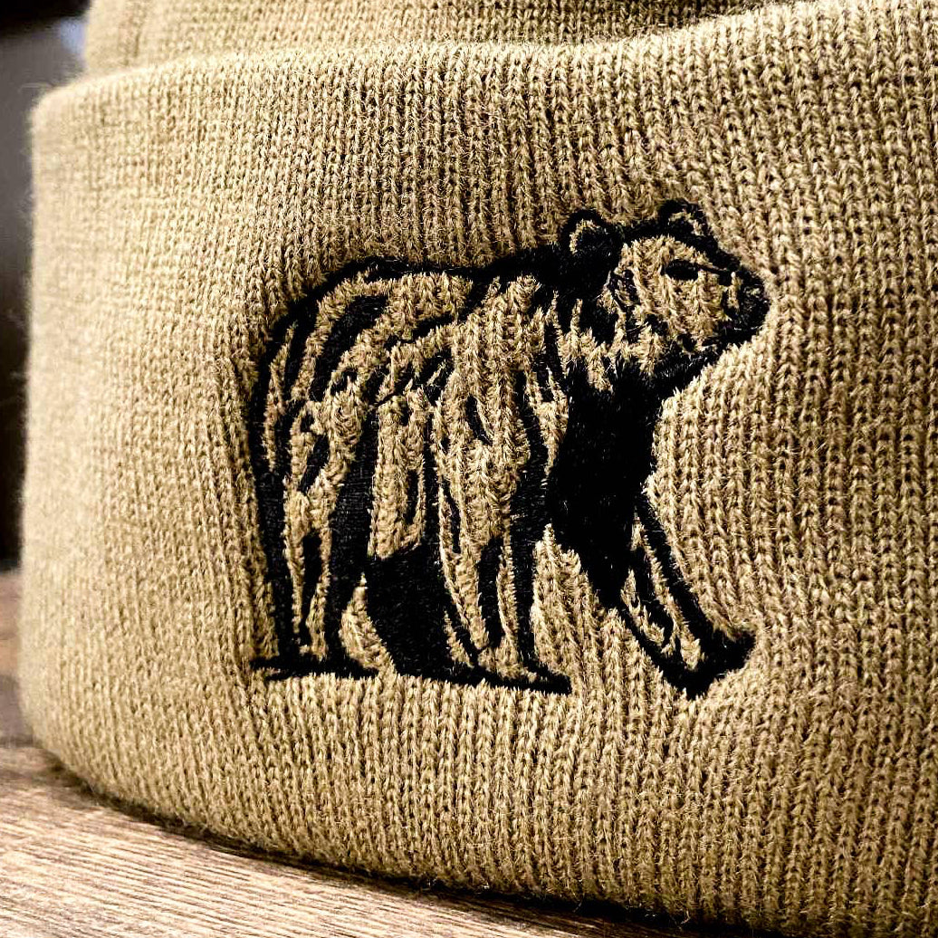 Beige beanie with bear embroidery and brand tag on a wooden surface