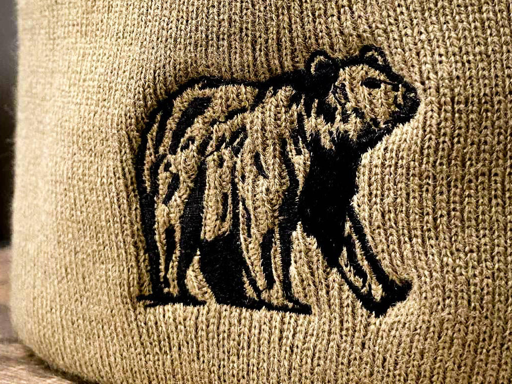 Beige beanie with bear embroidery and brand tag on a wooden surface