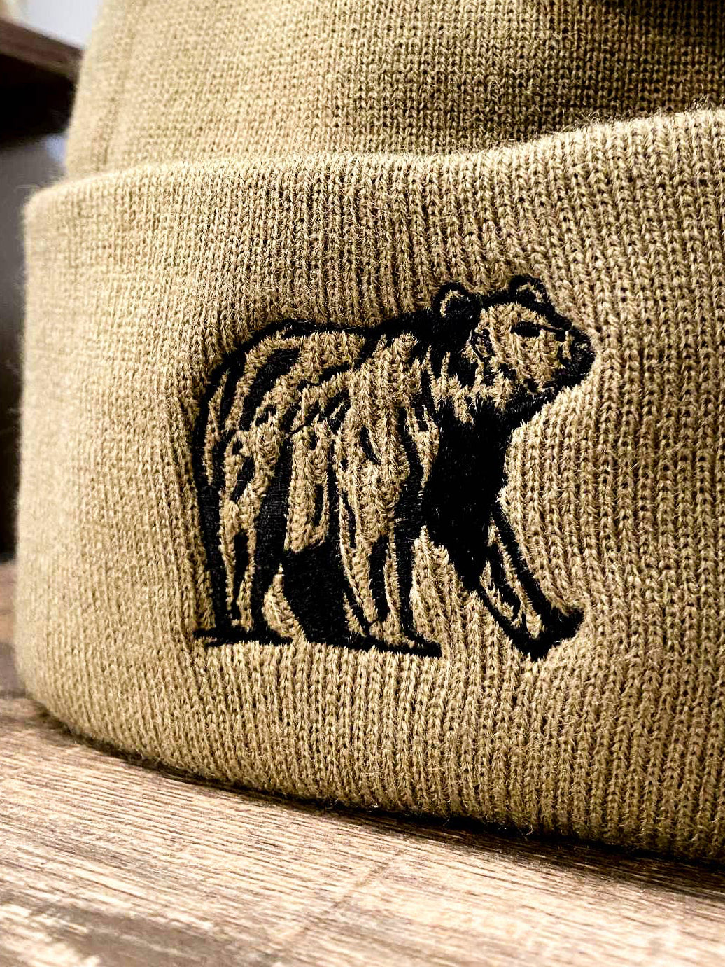 Beige beanie with bear embroidery and brand tag on a wooden surface