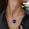 Gold necklace with a blue heart-shaped pendant worn by a person.