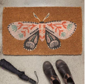 a doormat featuring a pretty moth staged at a door with shoes nearby